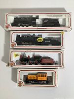 Four Bachmann HO scale electric model trains in original packaging arranged from top to bottom, showing engines and tenders along with a caboose.