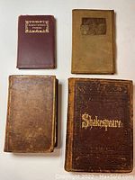 Four antique leather-bound books arranged on a white surface showing varied cover textures and titles