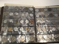 Coins displayed in clear plastic pockets inside a 3-ring binder, showing multiple rows of foreign coins primarily European.