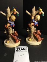 Front angle showing the two Hummel figurines side by side, depicting boy climbing tree and dog at base, with note card showing measurement.
