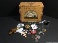 Photo of the entire lot showing letter opener, pins, lighters, cigar box and medallions arranged on black background.
