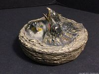 Metal bird nest trinket box with three baby birds, side angle showing detailed textured nest and birds with open beaks.