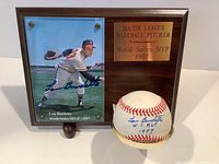 Photo of wooden plaque featuring signed Lou Burdette photograph, engraved brass plate noting 1957 World Series MVP, and signed baseball displayed in front on stand.