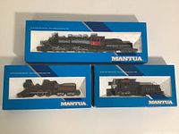 Three Mantua HO scale model trains in original blue packaging. Top train labeled 'Deep River Logging Co.' Logger with Tender. Middle train is Pennsylvania General with tender. Bottom train is L.H.R. Goat Switcher with tender. All boxed, viewed from above.