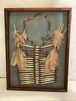 Full view of the framed ceremonial breast piece showing bone segments, feathers, and beads on a fabric background.