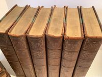Photo of spines of volumes showing the title 'Plutarch's Lives and Writings' and volume numbers, with ornate gilt designs and labels differentiating 'The Lives' and 'Essays and Miscellaneous'.