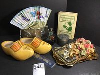 Full lot overview showing various keepsakes including wooden clogs, cookbook, metal trinket box, fan, and gold trays