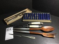 Overall photo showing all items including letter opener in box, salad servers, carving sets, corn cob holders, and small spreader knife.