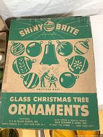 Original Shiny Brite cardboard box for glass Christmas tree ornaments. Green and tan box with vintage graphics and branding.