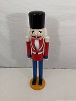 Front view of vintage wooden nutcracker soldier figurine standing upright on round base.