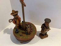 View showing music box with carved child figurine, deer, birds, mushrooms, and floral details on top with separate carved lawyer figurine.