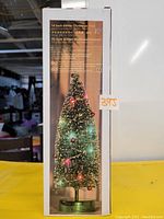 Photo of the box packaging showing the 14 inch green glitter Christmas tree with LED lights on and decorations.