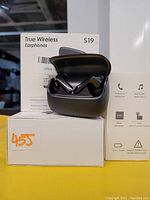 Photo of one open black charging case displaying two wireless earbuds, with the product box in background showing key features.