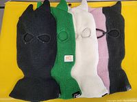 Photo of four knit ski masks lying flat on a yellow background, showing full head coverage and eye and mouth openings.