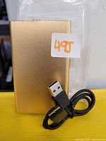 Gold external hard drive and USB cable shown against yellow surface with white background