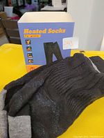 Blue box labeled 'Heated Socks for Winter' with black and grey heated socks in front showing ribbed detail and padded areas.