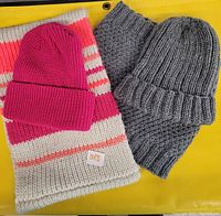 Two sets of neck warmers with matching toques: one pink toque with a cream, pink, and coral striped neck warmer; one grey toque with a grey neck warmer.