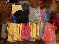 Overview of various folded and plastic-wrapped scrub tops and pants in multiple colors stacked on floor.