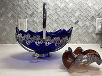 Front angle of cobalt blue glass fruit bowl with silver floral trim and base, alongside the Murano glass dish