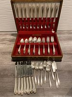 Full view of the cutlery set arranged in the open wooden box with red velvet and satin lining. Contains knives, forks, spoons, and butter knives.