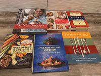 Top view showing all seven cookbooks arranged on a wooden surface including My New Orleans, Happy Cooking, French Chef Cookbook, The Gardener & The Grill, In & Out of the Kitchen, and A Year of the Best.