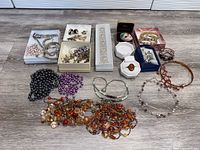 Wide view of multiple vintage costume jewelry pieces on floor including necklaces, bracelets, and earrings grouped mostly by type and color with some items in boxes.