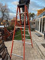 Full view of the Featherlite 8 foot step ladder standing on a paved outdoor surface, showing its height and orange color with silver steps.