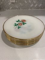 Stack of 8 white milk glass plates with pink roses and gold trim visible on edges, showing wear to gold rim.