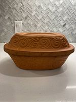 Side view of brown ceramic roaster with decorative swirl pattern lid, showing the entire roaster and lid design.