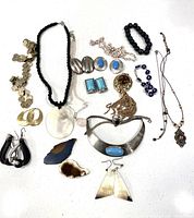 Photo showing full assortment of jewelry including necklaces, earrings, bracelets, pendants, and stones spread out on a white surface.
