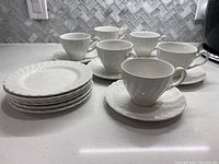 All items including 6 teacups on saucers and stack of 6 dessert plates on countertop