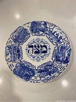 Top-down view of the round blue and white ceramic plate featuring Hebrew scripture and detailed Passover scenes in eight sections around the edge.