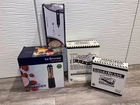 Photo showing boxed personal blender, milk frother, bagel cutter and replacement cartridge boxes on the floor against wall