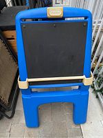 Front view of the Little Tykes drawing station showing blue frame, black chalkboard surface, and beige tray and clips