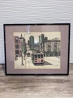 Framed cityscape etching showing a San Francisco cable car on San Francisco street, mounted with mauve matting and black frame.