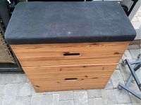 Front view of the wooden IKEA pommel horse style storage bench showing the dark cushioned seat on top and two wooden drawers with rectangular cut-out handles below it.