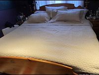 Full view of the king size bed covered with khaki quilted bed cover and two matching pillow shams on a wooden bed frame.