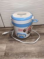 Front view of small electric rice cooker showing blue and white design and power cord