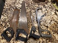 Four hand saws laid on granite surface; all show heavy rust; one is a hacksaw frame missing blade
