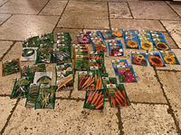 Wide overview of 39 unopened Burpee seed packets laid on stone floor, organized in rows showcasing vegetable, herb and flower seeds in colorful packaging.