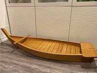 Full side angle of the large bamboo sushi boat showing length and structure on floor.