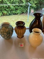 View of four urn style vases including dark brown tall vase, cream swirl patterned vase, amber ribbed vase, and teal leaf patterned vase