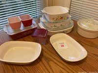Multiple vintage Pyrex and Anchor Hocking casserole dishes in various shapes, sizes, and colors arranged on wooden table.