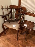 Padded accent chair with woven beige seat, cherry knick knack shelf with three tiers placed on chair, and cherry wooden plant stand beside chair