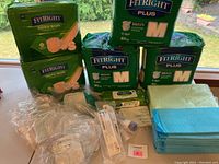 Multiple packs of FitRight Plus medium briefs, few opened and unopened, small cannulas, blue and green bed pads.