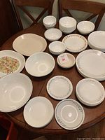 Photo of various mismatched Corelle dishware displayed on a wooden table showing different patterns, floral designs, and sizes including plates and bowls.