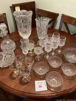 Overview of all crystal pieces on a wooden table including decanters, stemware, vases, and bowls.