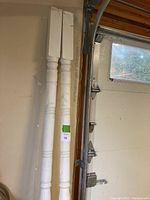 Pair of tall white wooden decorative posts leaning against a wall, visible dirt and wear.