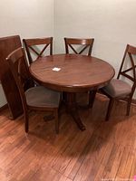 Full view of round dining table with 4 matching upholstered chairs around it on hardwood floor.
