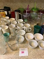 Wide view showing various mugs, travel mugs, plastic tumblers, ceramic mugs with designs, and clear glass cups.
